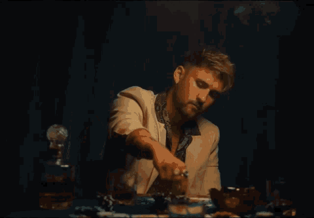 a man sits at a table with a decanter of whiskey and playing cards with the word " okay " on the table