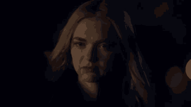 a woman with blonde hair is standing in the dark looking at the camera .