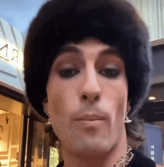 a man wearing a fur hat and earrings is making a face .