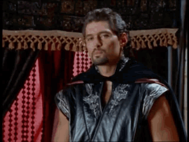 a man in a black cape is standing in front of a curtain
