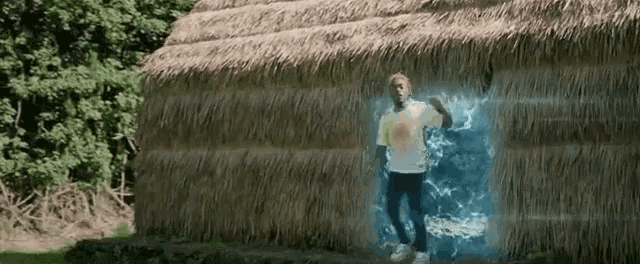 a man is standing in front of a thatched building with a blue light coming out of it .