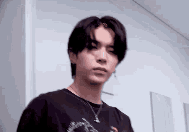 a young man wearing a black shirt and a necklace is standing in a hallway .