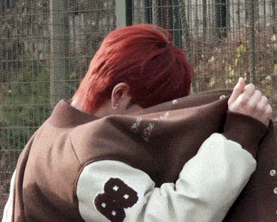 a person with red hair wearing a jacket with the letter b on the sleeve