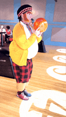 a man in a yellow sweater is holding a bowling ball in a bowling alley