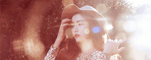 a woman wearing a hat and a floral shirt is standing in the sun
