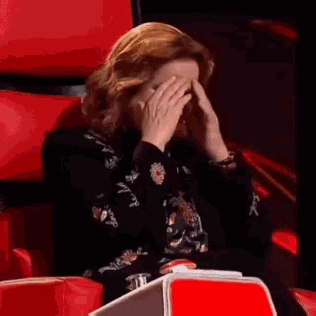 a woman covering her face with her hands while sitting in a red chair .