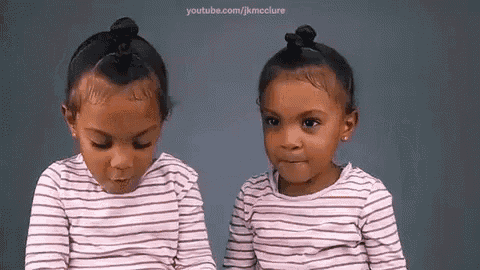 two little girls are sitting next to each other wearing striped shirts and making funny faces .
