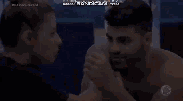 a man and a woman are arm wrestling and the woman is touching the man 's face .