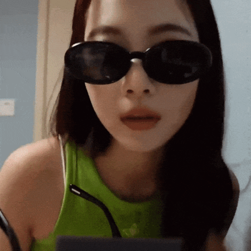 a woman wearing sunglasses and a green tank top looks at the camera