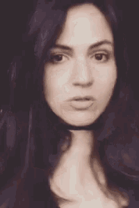 a woman with long black hair is wearing a choker around her neck and looking at the camera .