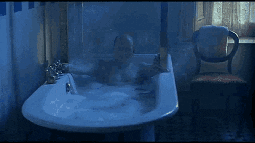 a man is taking a bath in a bathtub with a chair in the background