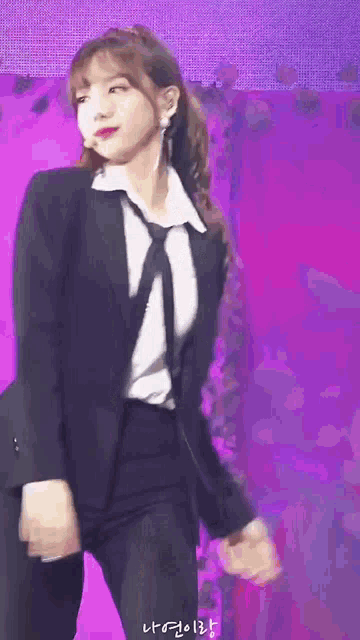 a woman in a suit and tie is dancing on a stage with a purple background .