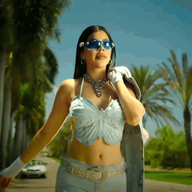 a woman wearing a butterfly top and sunglasses stands on a street