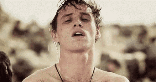 a shirtless man is sweating while standing on a beach with his eyes closed .