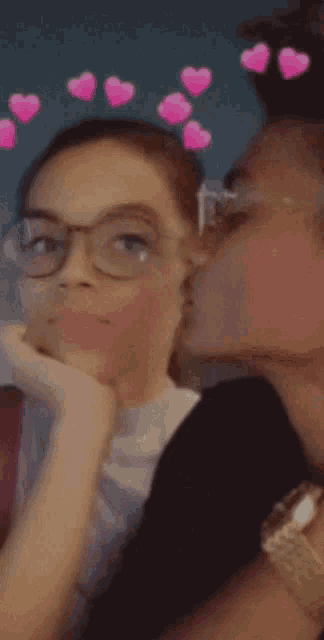a woman kissing another woman on the cheek with pink hearts on her head