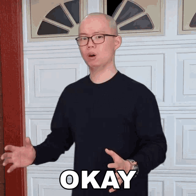 a bald man wearing glasses says okay in front of a white garage door