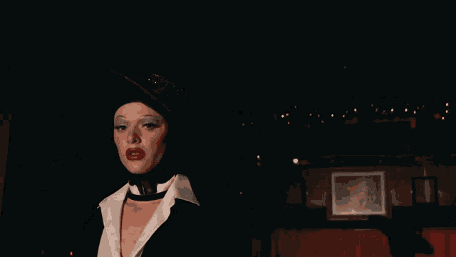 a woman with red lips and a black hat is standing in a dark room