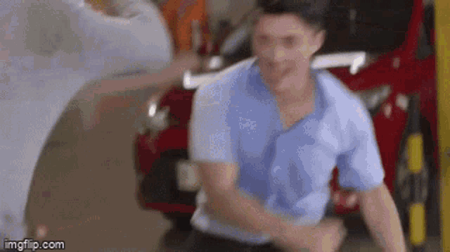 a man in a blue shirt is standing in front of a red car in a parking lot .