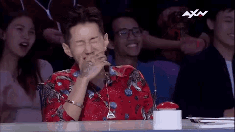 a man in a red shirt is sitting at a table with his eyes closed and laughing .