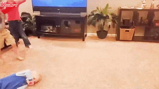 a baby is laying on the floor in a living room while a woman is dancing in front of a television .