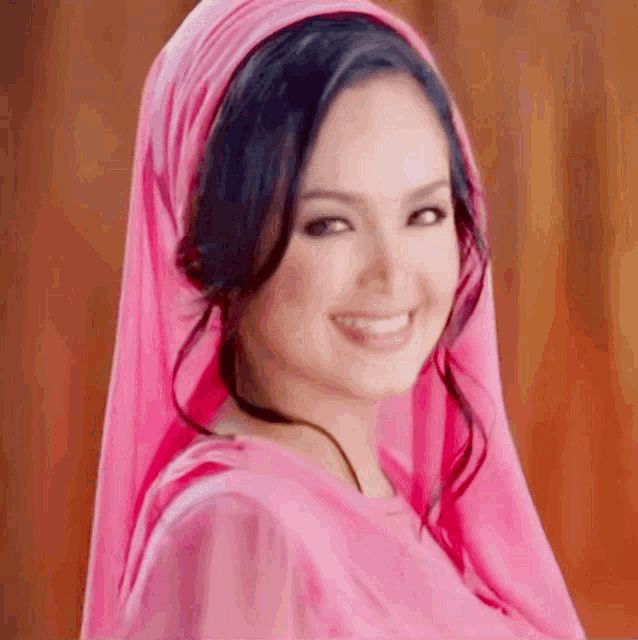 a woman wearing a pink head scarf and a pink dress is smiling .