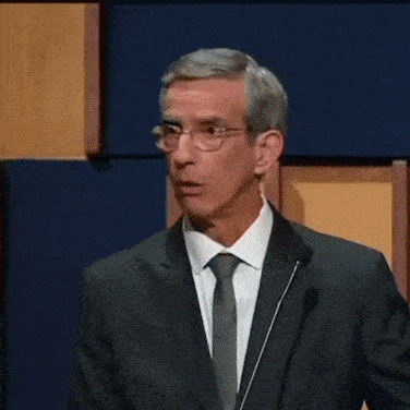 a man in a suit and tie is standing in front of a microphone and giving a speech .