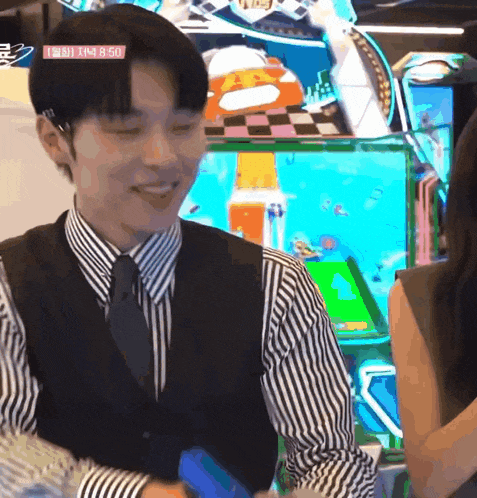 a man in a suit and tie is smiling in front of an arcade machine