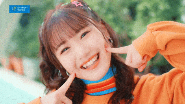 a girl in an orange sweater is smiling and making a funny face with her fingers