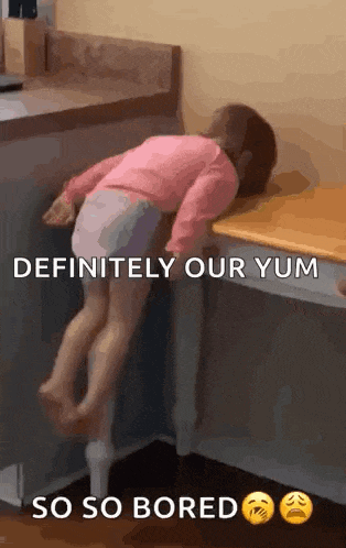 a little girl is laying on a table with a caption that says definitely our yum so so bored