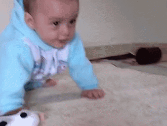 a baby in a blue hoodie is crawling on a blanket .