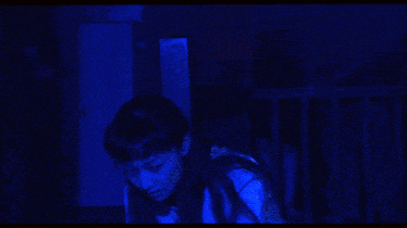 a man without a shirt is standing in a dark room with blue lights behind him
