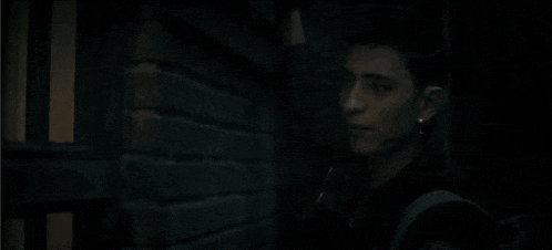 a man in a suit stands in front of a dark brick wall