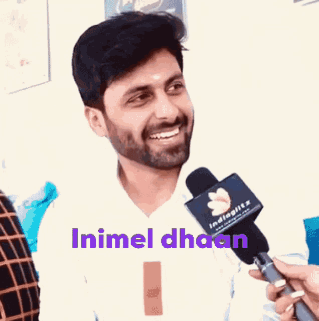 a man with a beard is smiling while holding a microphone with the words inimel dhaan written above him