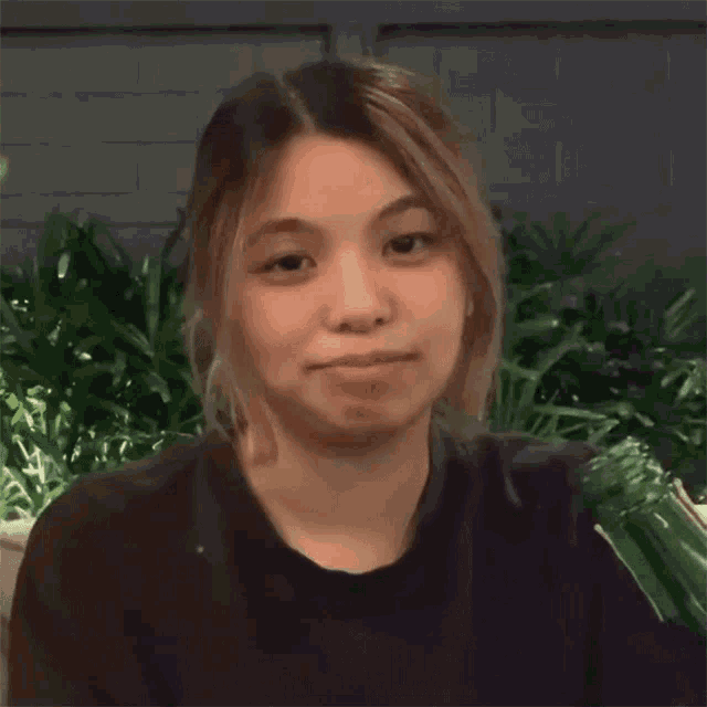 a woman in a black shirt is making a funny face while sitting in front of plants .