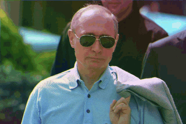 a man wearing sunglasses and a blue shirt has a jacket over his shoulder