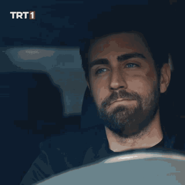 a man with a beard is smiling in a car with trt1 written in red