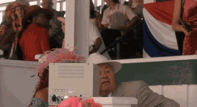 a man in a suit and cowboy hat sits in front of a white box that says ' lg ' on it