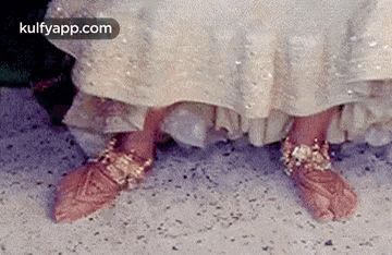 a close up of a woman 's feet wearing a white dress and gold jewelry .