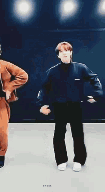 a man in a black sweater is dancing on a stage in a dark room .