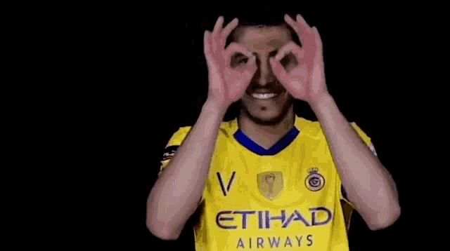 a soccer player wearing a yellow etihad airways jersey is making a funny face .