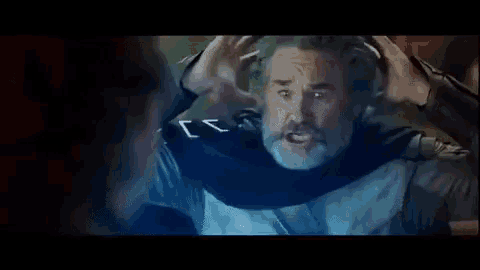 a man with a beard and mustache is wearing a cape and holding his hands to his head .