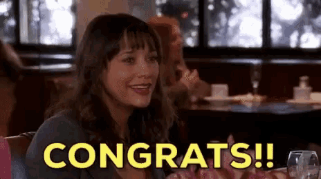 a woman is sitting at a table in a restaurant and smiling with the words congrats !