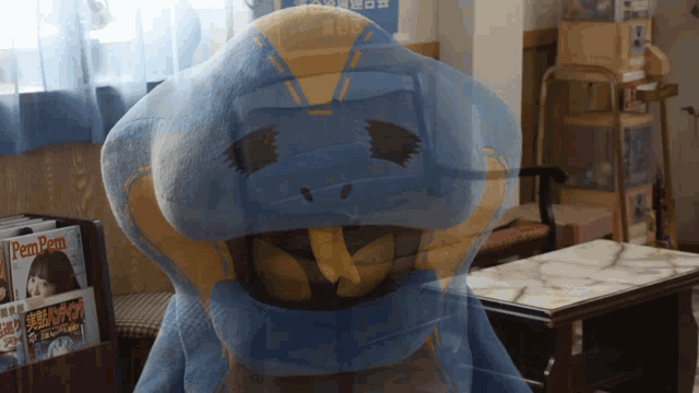 a blue and yellow stuffed animal is sitting in front of a bookshelf with pamper magazines on it