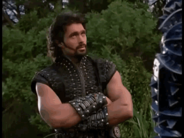 a man with his arms crossed is standing in front of a tree .