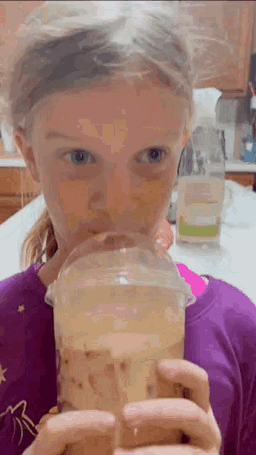 a young girl in a purple shirt is drinking from a cup .
