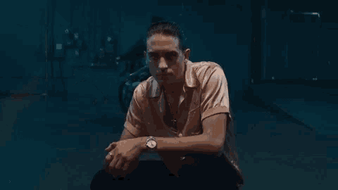 a man wearing a watch is sitting on the ground in front of a motorcycle in a dark room .