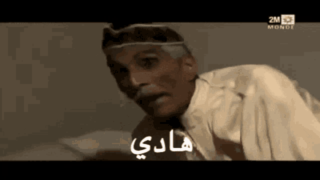 a man with a mustache and a crown on his head is laying on a bed with arabic writing behind him