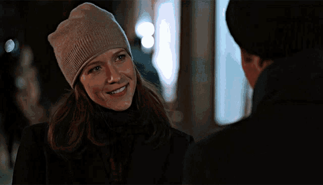 a woman wearing a beanie smiles at a man in a black coat