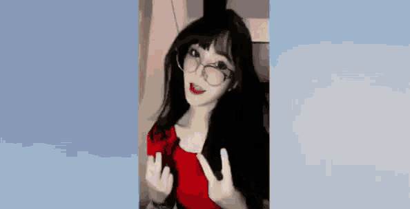 a woman wearing glasses and a red shirt is making a peace sign .