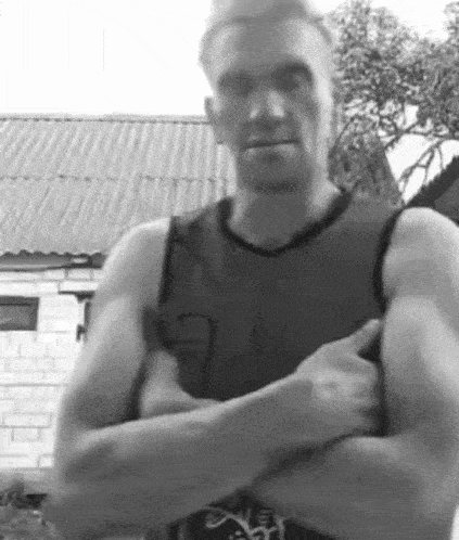 a man in a tank top is standing with his arms crossed and pointing at the camera .